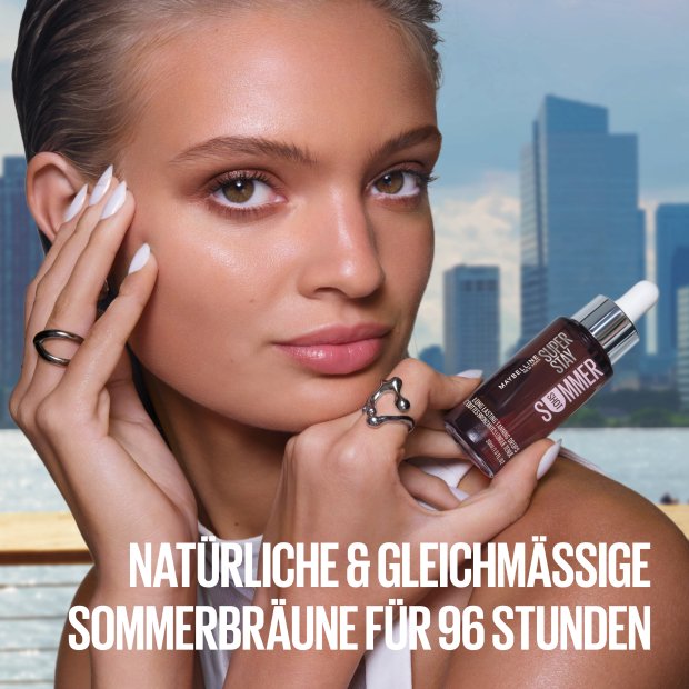 Frau, die die Maybelline Super Stay Tanning Drops in ihrer Hand hält, ihre andere Hand an der Schläfe.