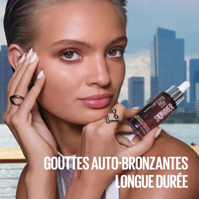 Une femme tenant le flacon de Maybelline Super Stay Tanning Drops dans une main, l'autre main posée sur sa tempe.