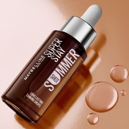 Flacon Super Stay Summer Shot de Maybelline sur fond bronze brillant avec des gouttes de sérum.